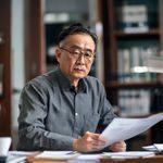 资深调查编辑陈磊的工作照，戴眼镜的中年男性正在认真审阅文件，背景为整洁的编辑室环境，专业严谨气质突出